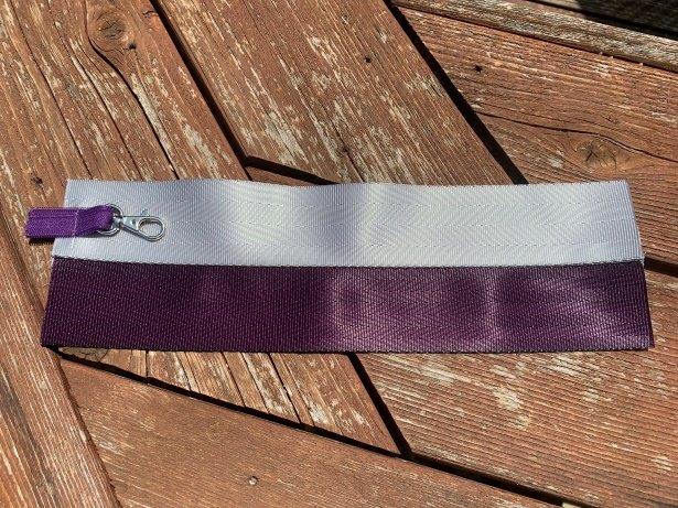 Two strips of seat belt webbing lay on wood surface. On the left side of the webbing lies a swivel clip facing toward center